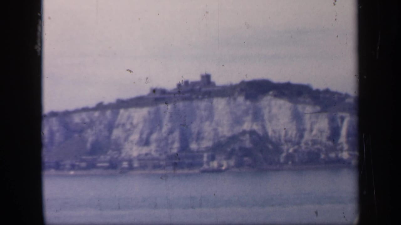 Dover cliffs and ridge-top castle appear in a soft 8mm frame, with muted sky and water in the foreground.
