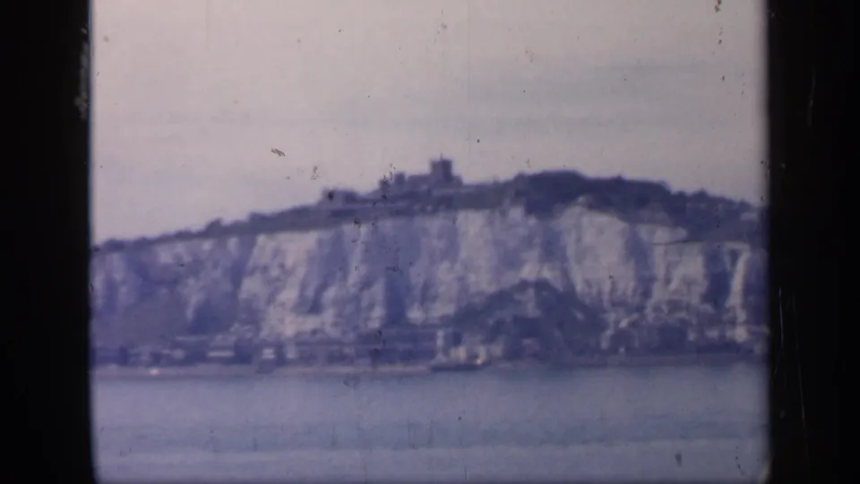 Dover cliffs and ridge-top castle appear in a soft 8mm frame, with muted sky and water in the foreground.