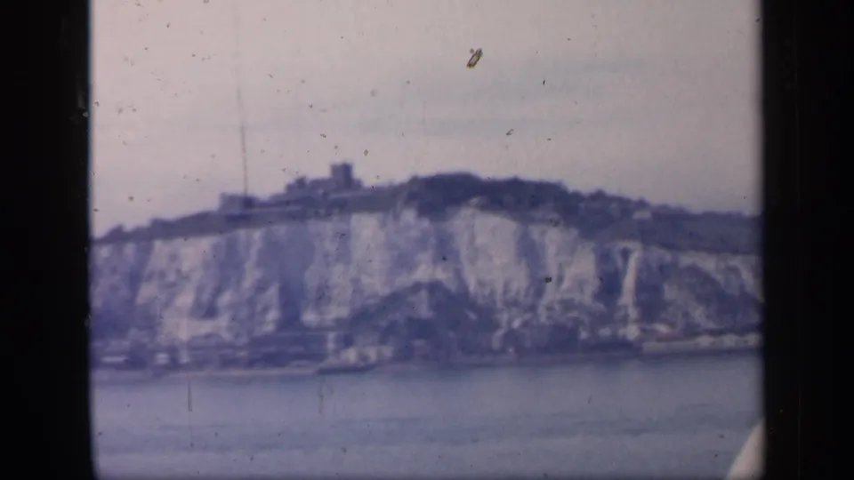 1949 England home-movie frame showing likely Dover chalk cliffs viewed from offshore, with a castle-like structure on the ridge.