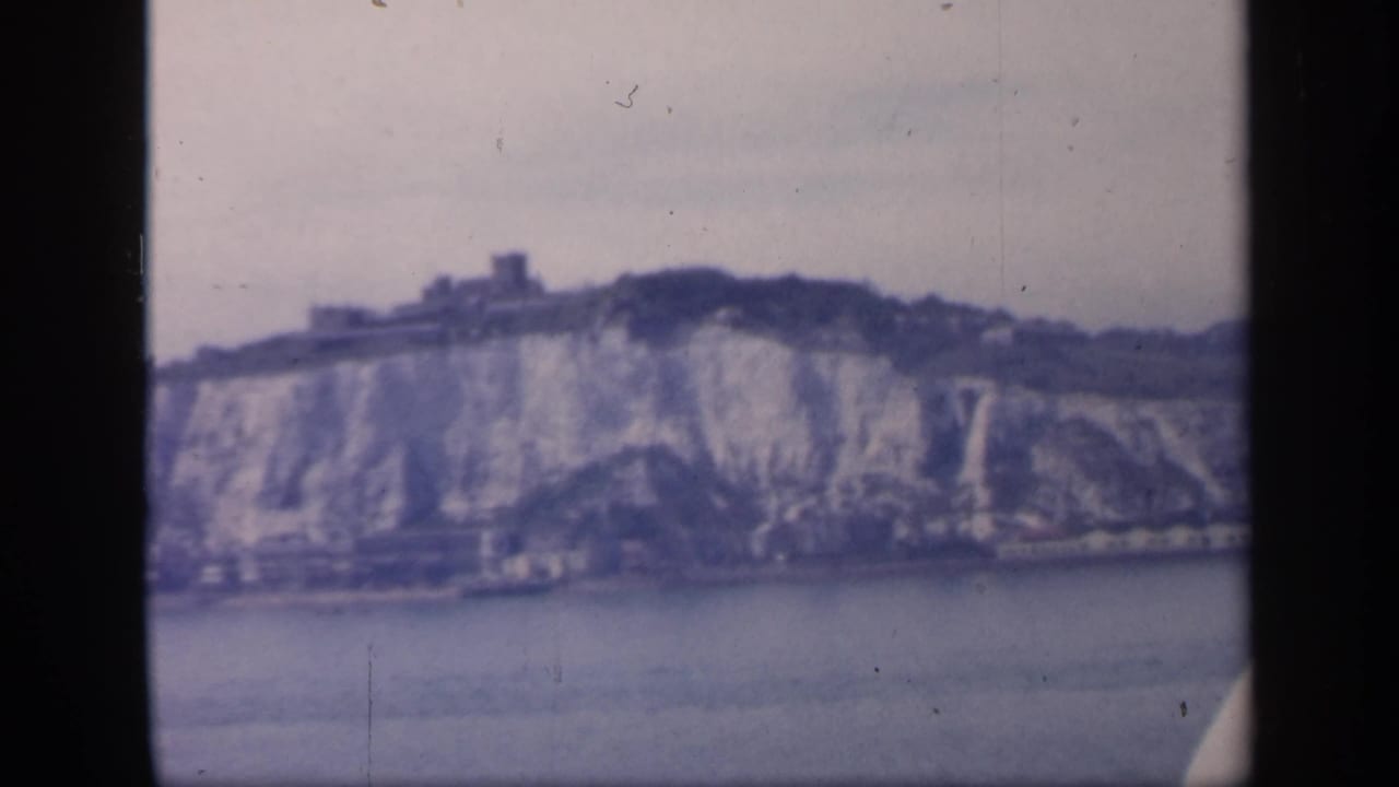 Likely Dover coastal cliffs in soft 8mm color, seen from a vessel with waterfront buildings at the cliff base.