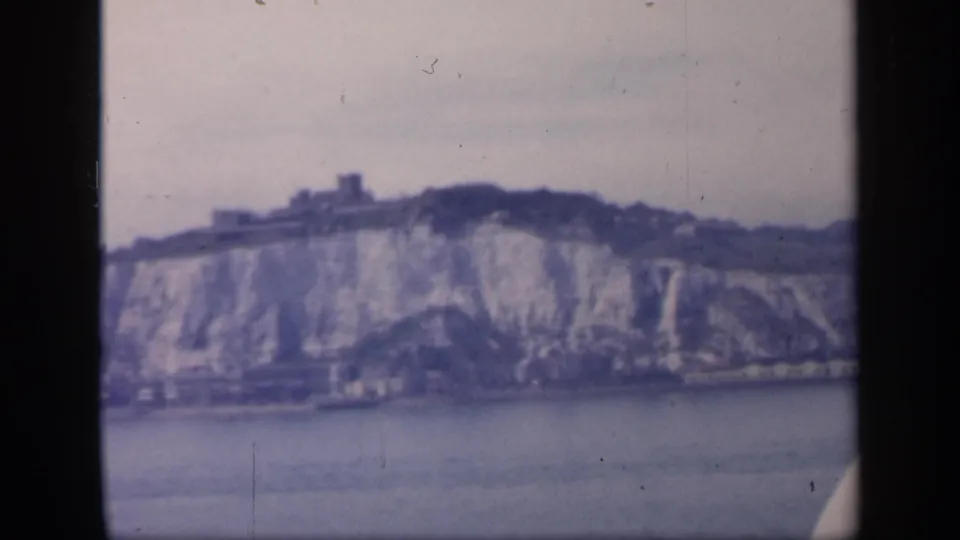 Likely Dover coastal cliffs in soft 8mm color, seen from a vessel with waterfront buildings at the cliff base.