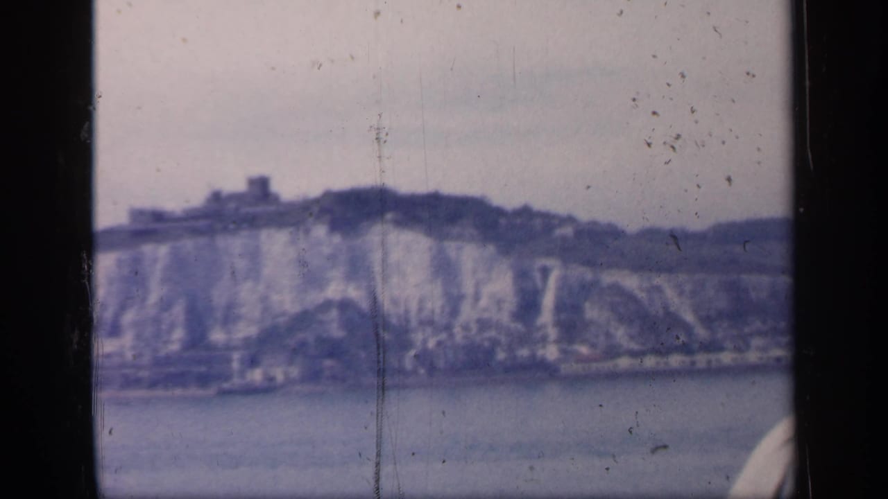 Archival 8mm frame of likely Dover cliffs from the water, with a castle-like feature on the ridge and soft faded color.