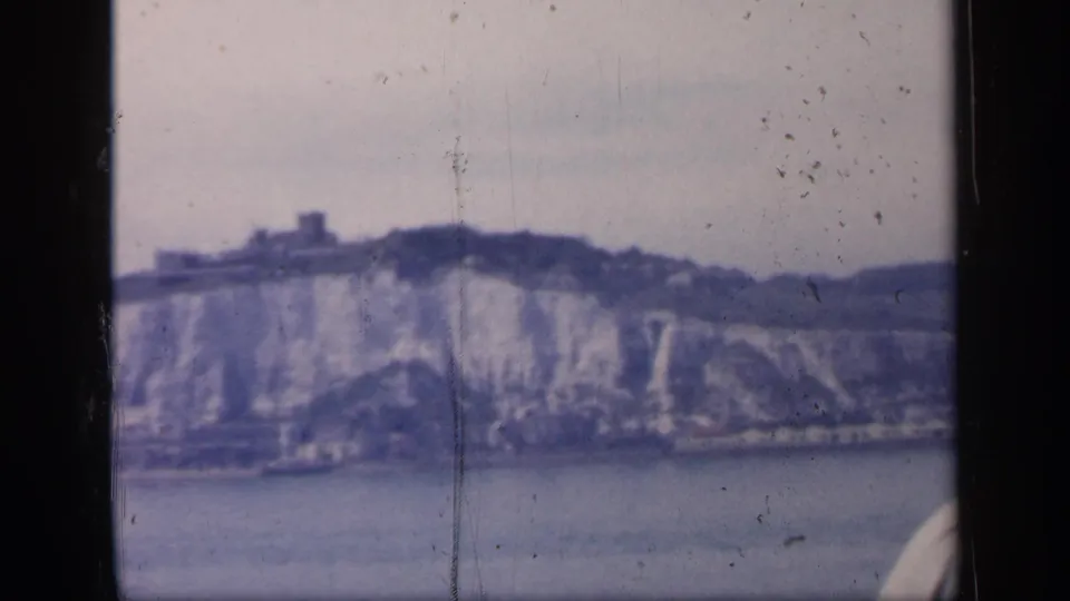 Archival 8mm frame of likely Dover cliffs from the water, with a castle-like feature on the ridge and soft faded color.