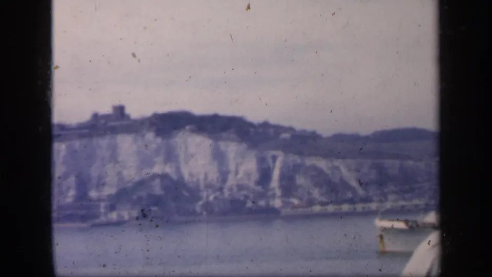 1949 England coastal frame with chalk cliffs in the distance and a small boat entering along the right edge of the water.