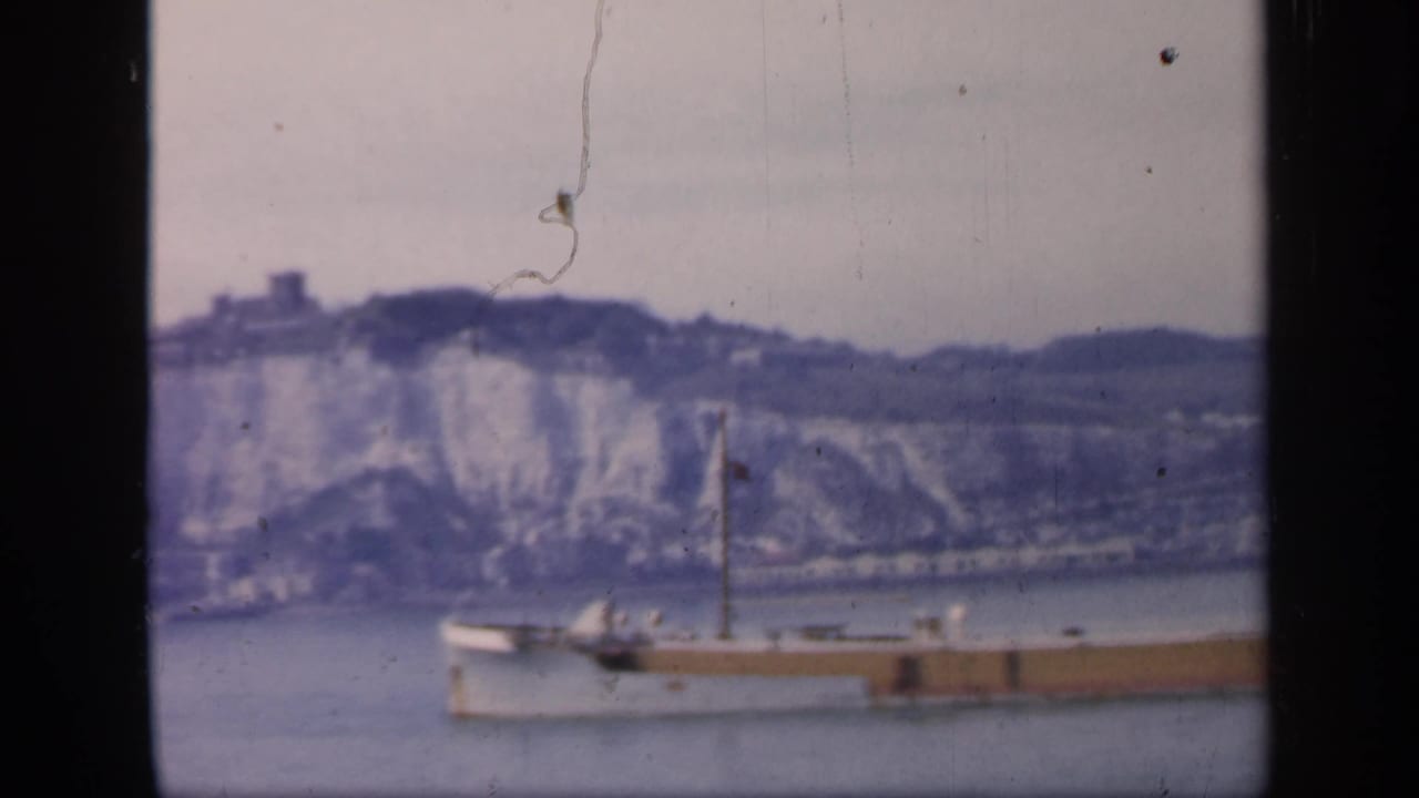 1949 England home-movie frame of a ship crossing the water, divided by a dark window frame, with white cliffs in the background.