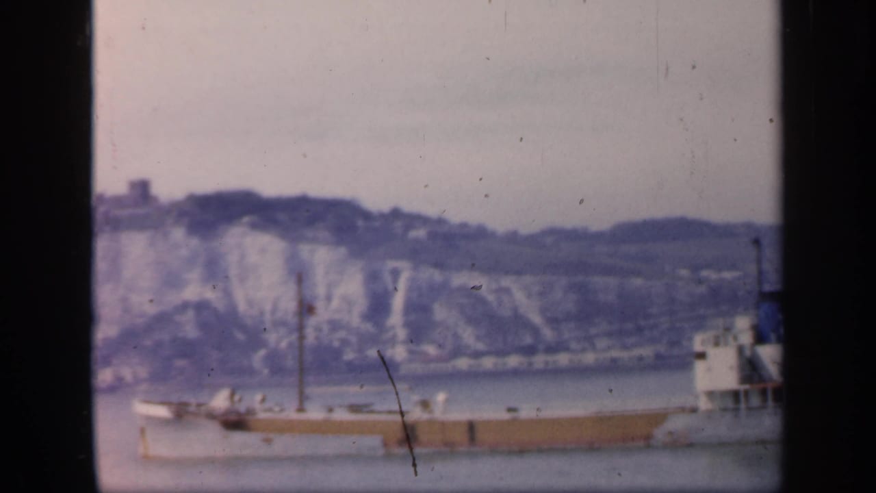 Soft 8mm frame from 1949 England showing the midsection of a large ship moving past pale cliffs and a distant hillside.