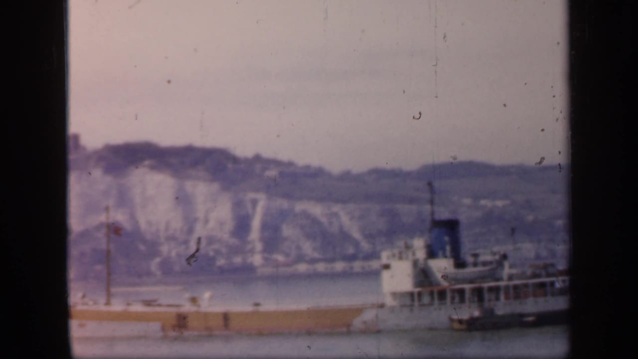 1949 England 8mm frame showing the rear section of a large vessel moving past white cliffs under an overcast sky.