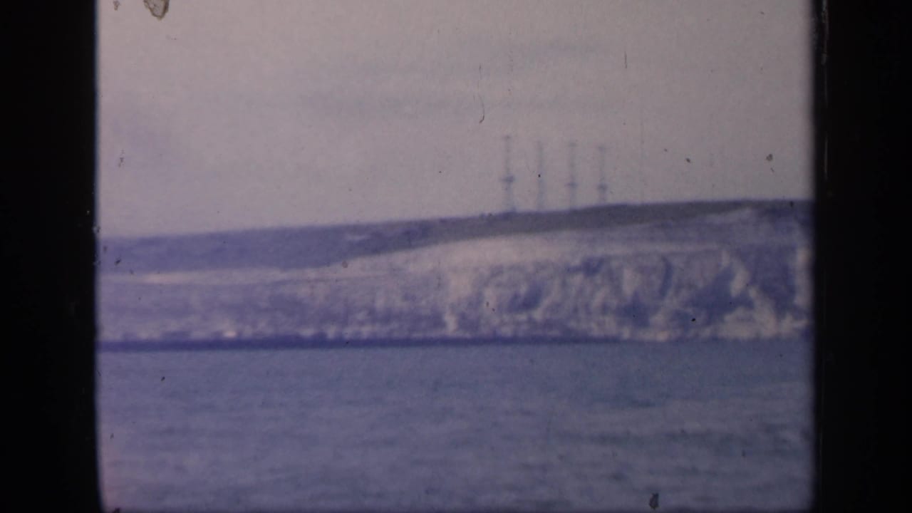 Distant pale coastal cliff across water with towers on the ridge and black 8mm frame edges.