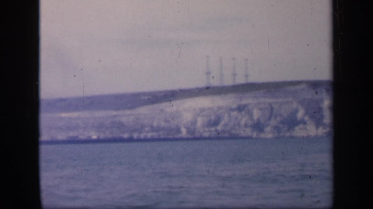 1949 England coastal view on 8mm film, holding on a distant white cliff, sea foreground, and faint towers along the skyline.