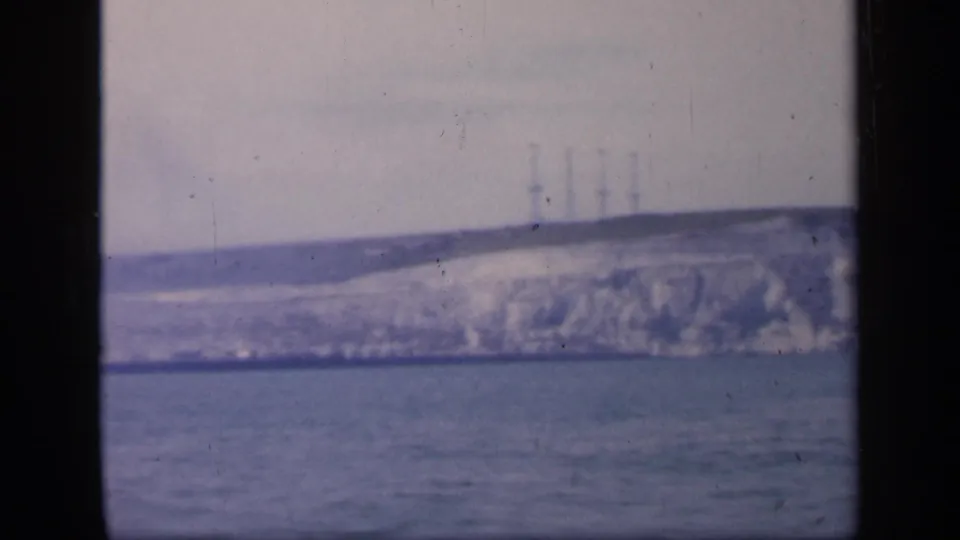 1949 England coastal view on 8mm film, holding on a distant white cliff, sea foreground, and faint towers along the skyline.