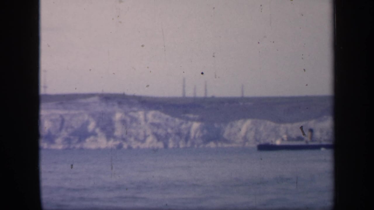 1949 England coastal view with a dark ship passing below pale chalk cliffs, framed by a central vertical window division.