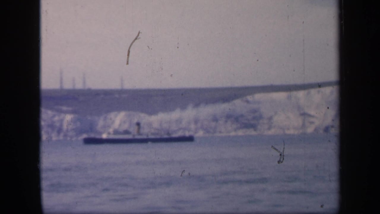 1949 England 8mm frame showing white chalk cliffs beyond open water, with a low dark boat crossing the foreground.