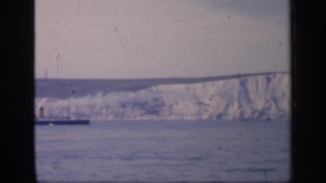 Distant white cliffs and sea with part of a small dark vessel near the horizon.