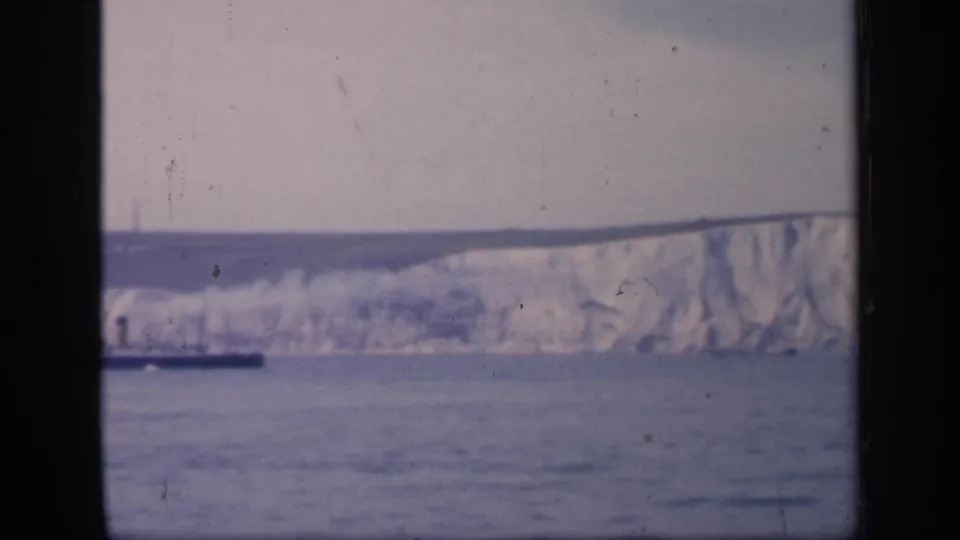 1949 England coastal view with chalk cliffs, open water, pale sky, and a small dark vessel partly visible near the horizon.