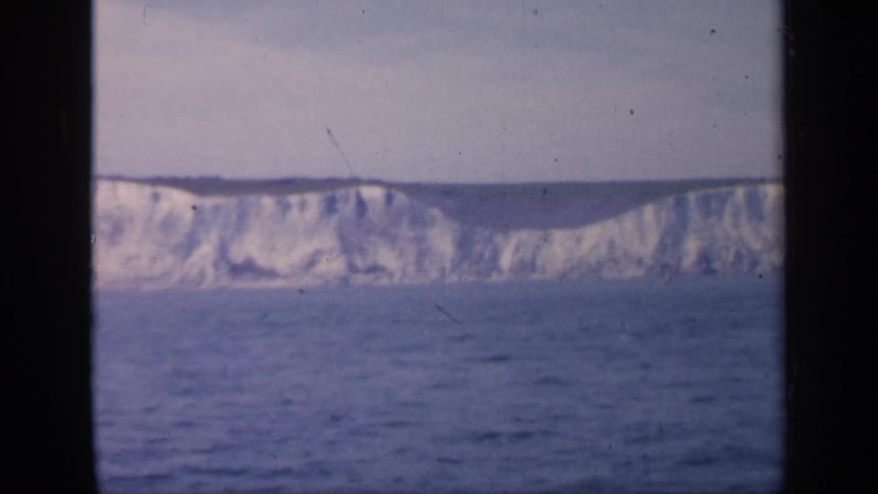 1949 England coastal frame with white chalk cliffs, open sea, pale sky, and visible 8mm film wear at the edges.