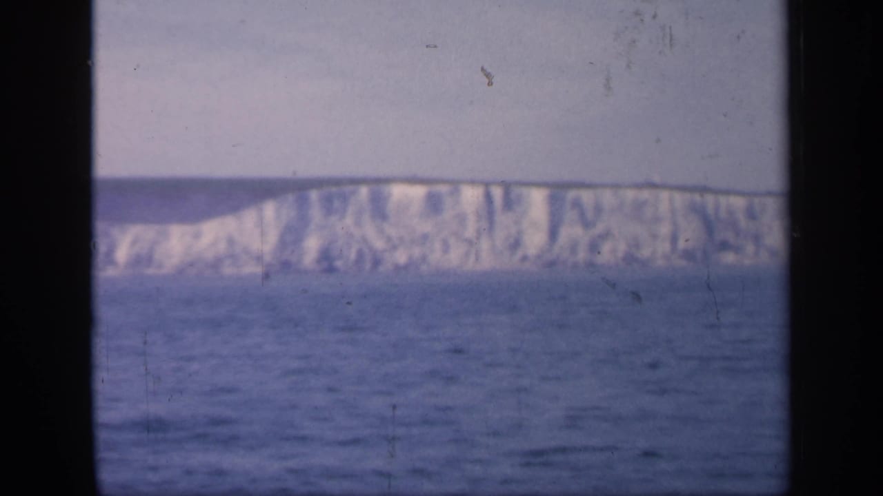 A long white cliff face rises beyond the sea, viewed through a vertical window divider.