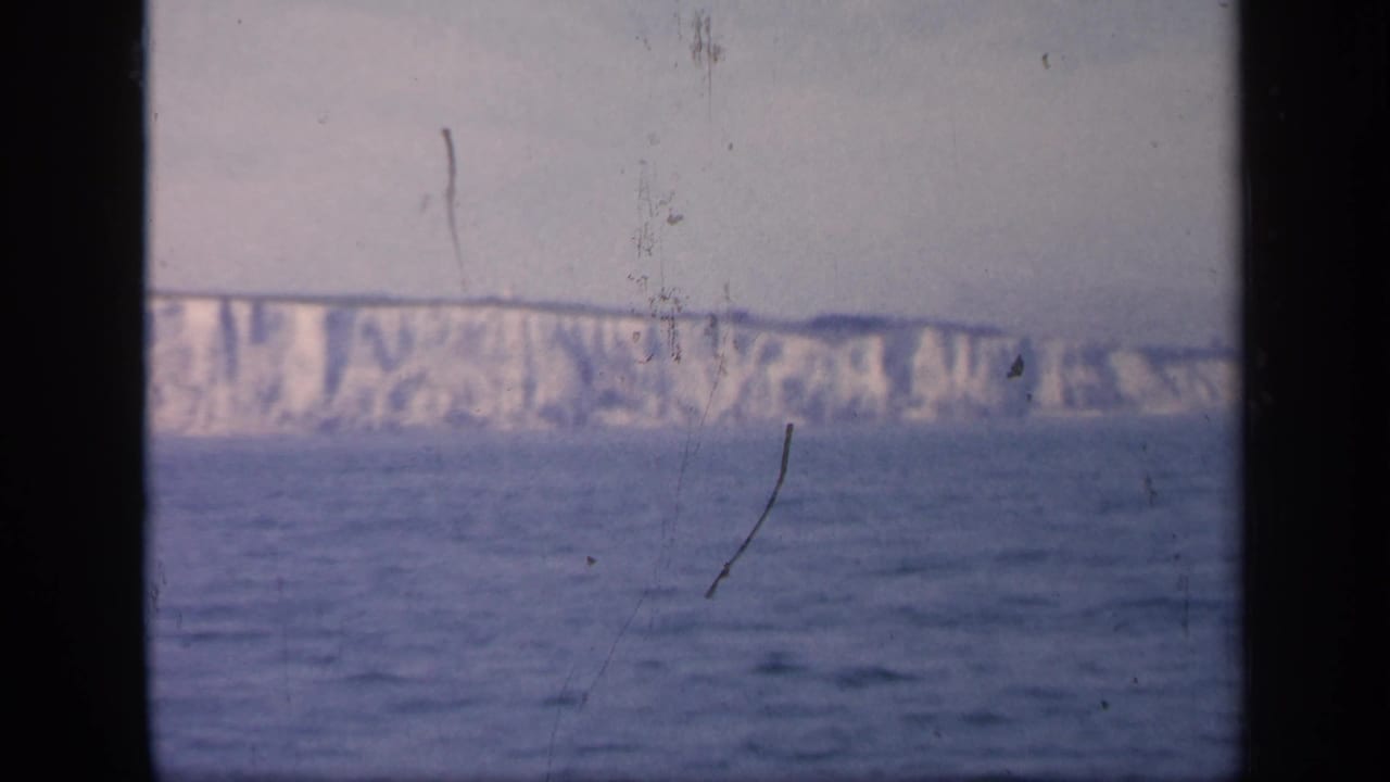Distant white cliffs across the sea, seen through a dark ship-window frame.