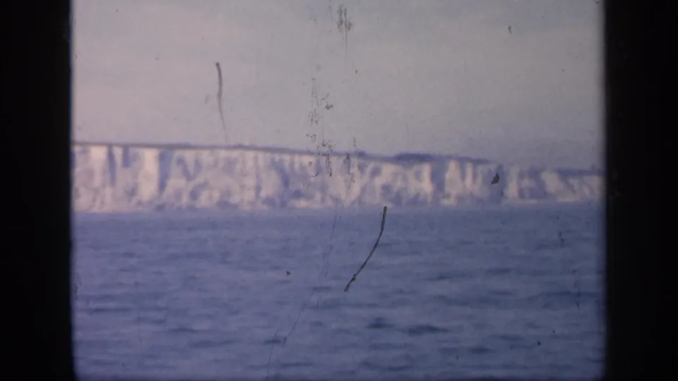 1949 England home-movie frame showing the Dover cliffs across open water, divided by dark window framing and visible film scratches.