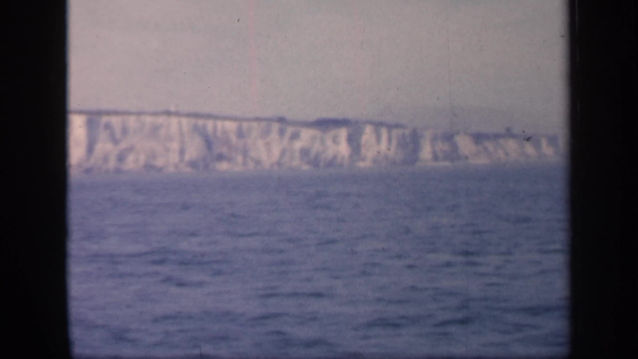 Soft 8mm view of the Dover cliffs from offshore, with open sea in the foreground and dark film or window framing at the sides.