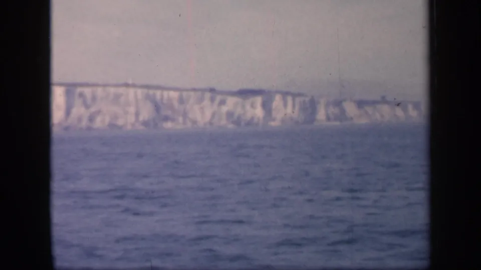Soft 8mm view of the Dover cliffs from offshore, with open sea in the foreground and dark film or window framing at the sides.