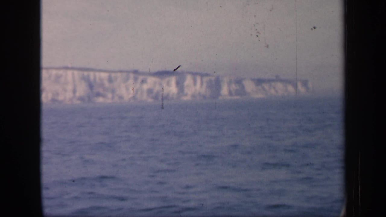 1949 England 8mm frame showing distant chalk cliffs beyond the sea, with soft color, grain, and dark projector-style edges.