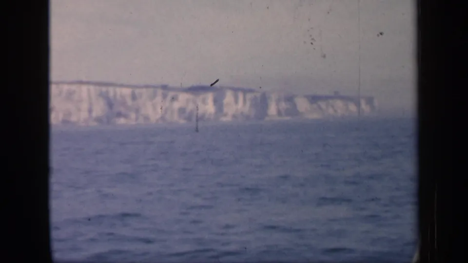 1949 England 8mm frame showing distant chalk cliffs beyond the sea, with soft color, grain, and dark projector-style edges.