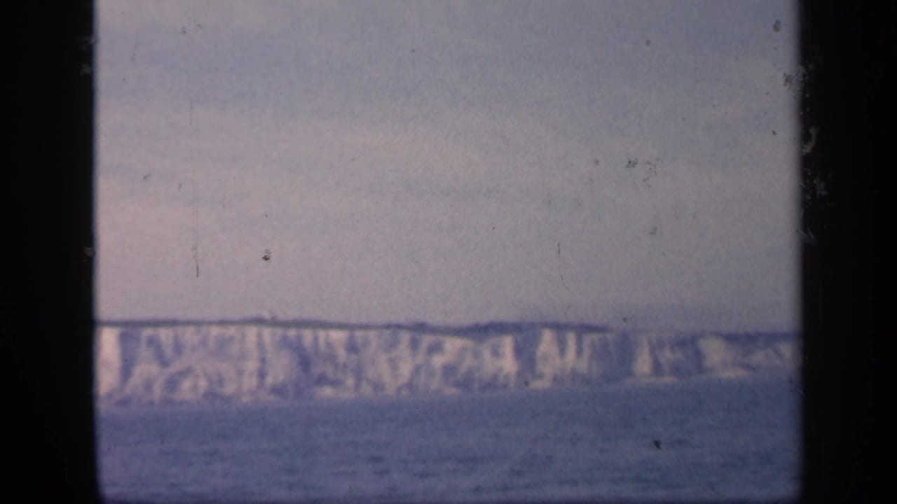 White cliff line on the horizon above calm water, with a dark vertical frame edge at left.