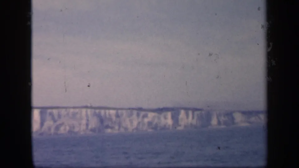 A distant English chalk coastline sits above the sea in this 1949 8mm home-movie frame, bordered by dark film-gate edges.