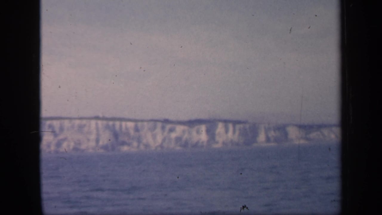 The final sampled frame holds on the English cliff coastline from across the water, with grain, muted color, and gate-edge borders.