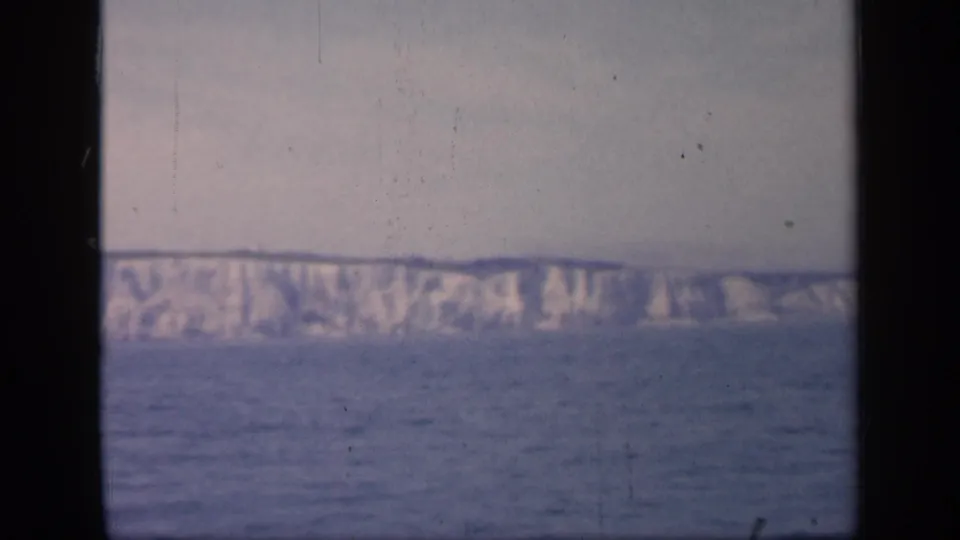 1949 England 8mm frame showing distant white cliffs beyond open water, with dark film borders and a soft hazy sky.
