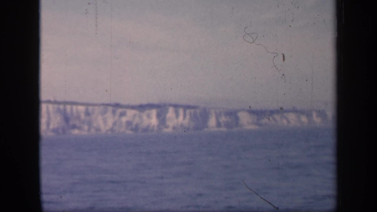 1949 England coastline frame with chalky cliffs stretching across the horizon above blue water and visible 8mm frame edges.