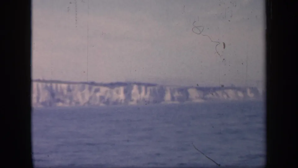 1949 England coastline frame with chalky cliffs stretching across the horizon above blue water and visible 8mm frame edges.