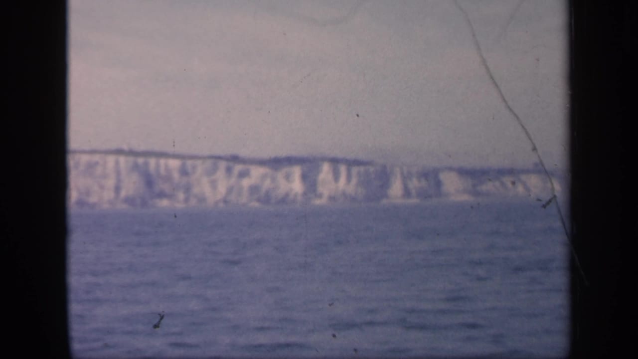 1949 England offshore view with pale cliffs, blue-gray sea, soft focus, and a visible scratch running through the 8mm frame.