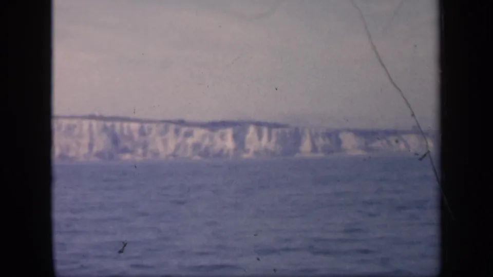 1949 England offshore view with pale cliffs, blue-gray sea, soft focus, and a visible scratch running through the 8mm frame.