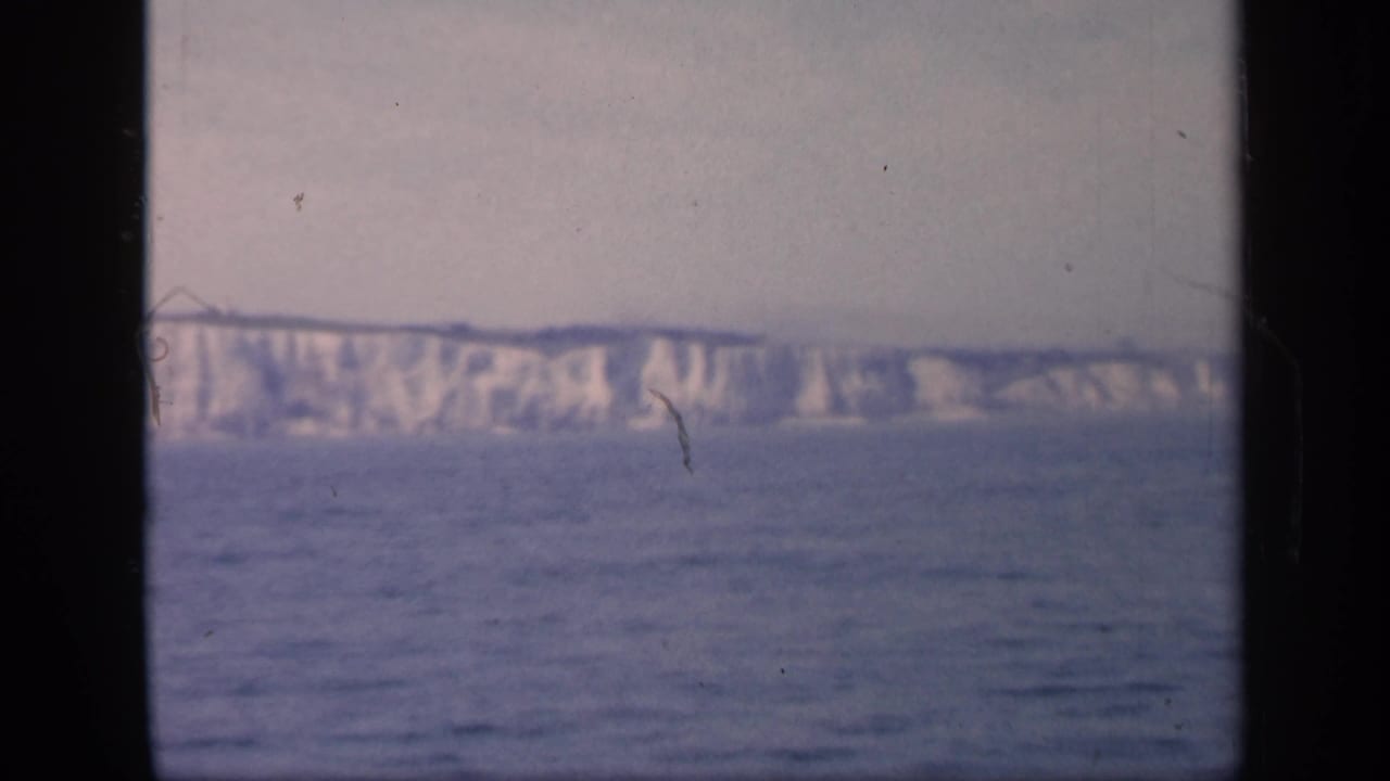 1949 England 8mm frame showing a broad white cliff face across open water, with muted color and small dust or scratch marks.