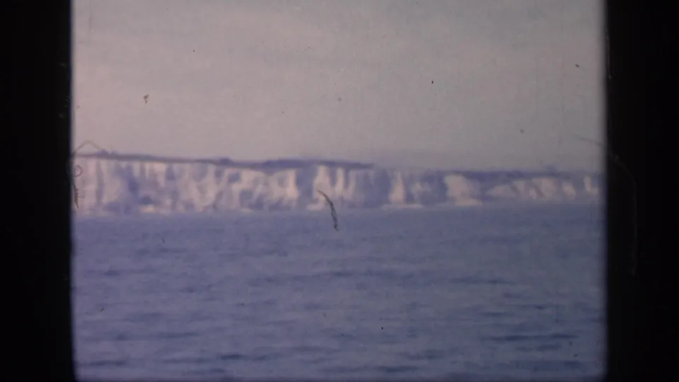 1949 England 8mm frame showing a broad white cliff face across open water, with muted color and small dust or scratch marks.