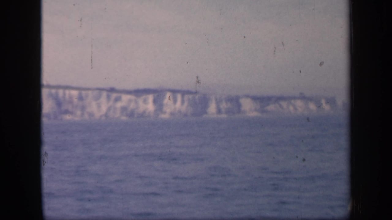 White chalk cliffs across calm water under a pale sky.
