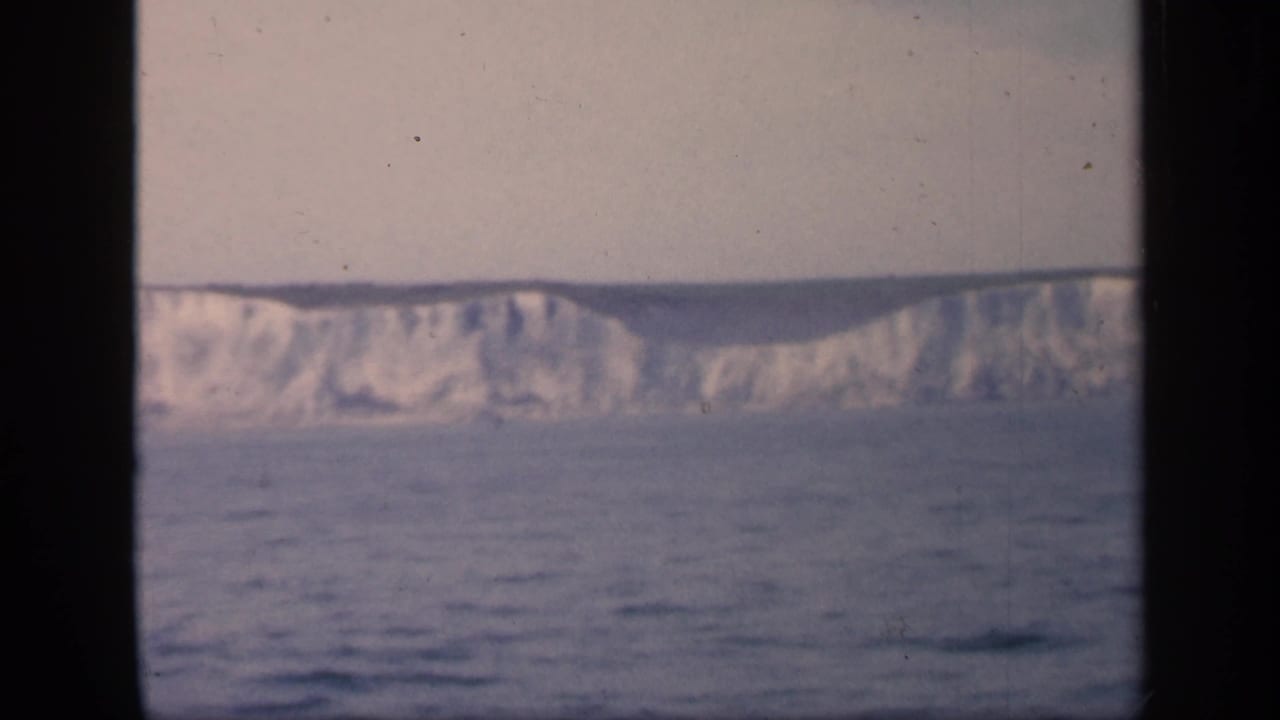1949 England home-movie frame showing pale chalk cliffs beyond open water, partly divided by dark boat-window bars.