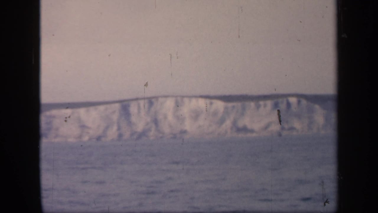 Distant English coastal cliffs stretch across the horizon, filmed from behind dark vertical window framing.