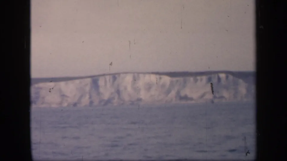 Distant English coastal cliffs stretch across the horizon, filmed from behind dark vertical window framing.