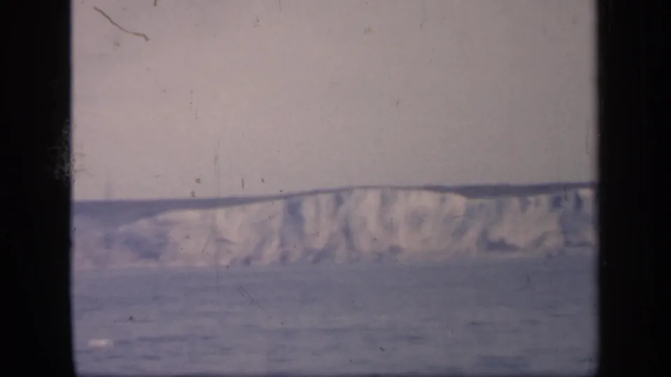 1949 England home-movie frame showing a distant pale cliff or hillside above water, with soft focus and visible film gate edges.