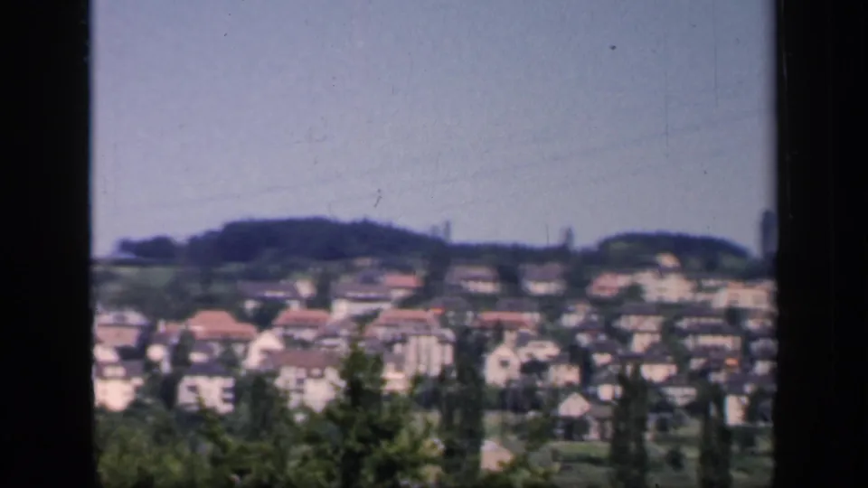 1949 England hillside town view with rows of houses, red roofs, trees, and a distant tower-like shape on the skyline.