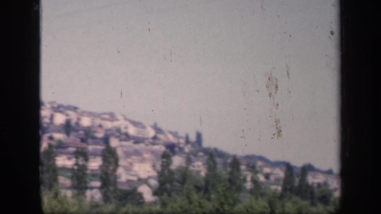 1949 England home-movie frame with hillside houses, scattered trees, clear sky, and a dark vertical strip from the film contact view.