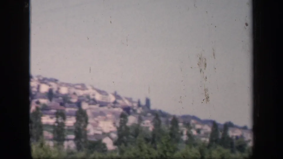 1949 England home-movie frame with hillside houses, scattered trees, clear sky, and a dark vertical strip from the film contact view.
