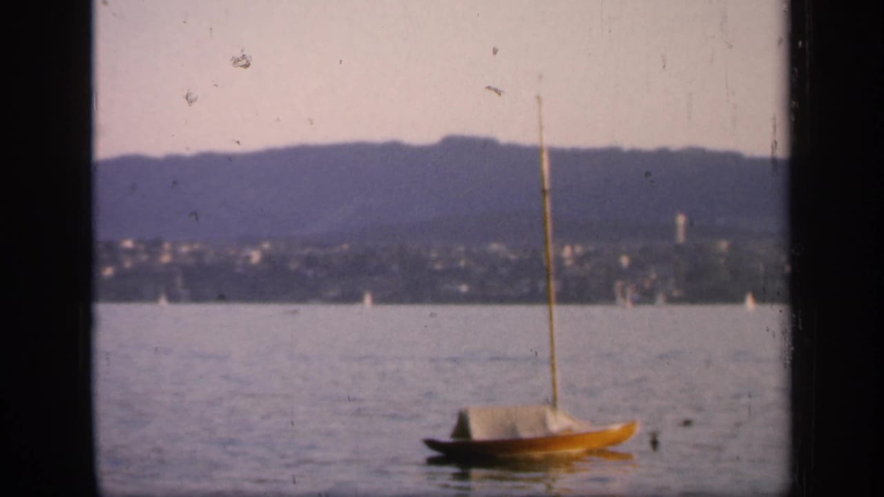 Yellow sailboat floating on calm water with distant hills and shoreline behind it.