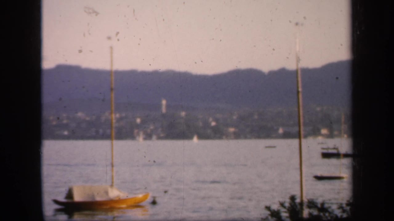 1949 England home-movie view of a yellow sailboat near the foreground, with calm water, far hills, and scattered boats behind it.