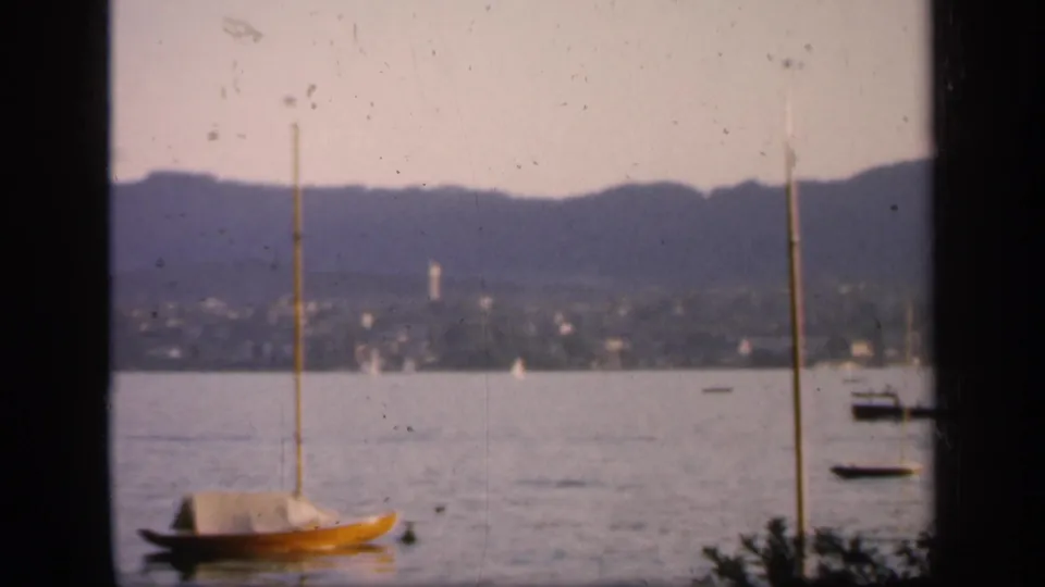 1949 England home-movie view of a yellow sailboat near the foreground, with calm water, far hills, and scattered boats behind it.