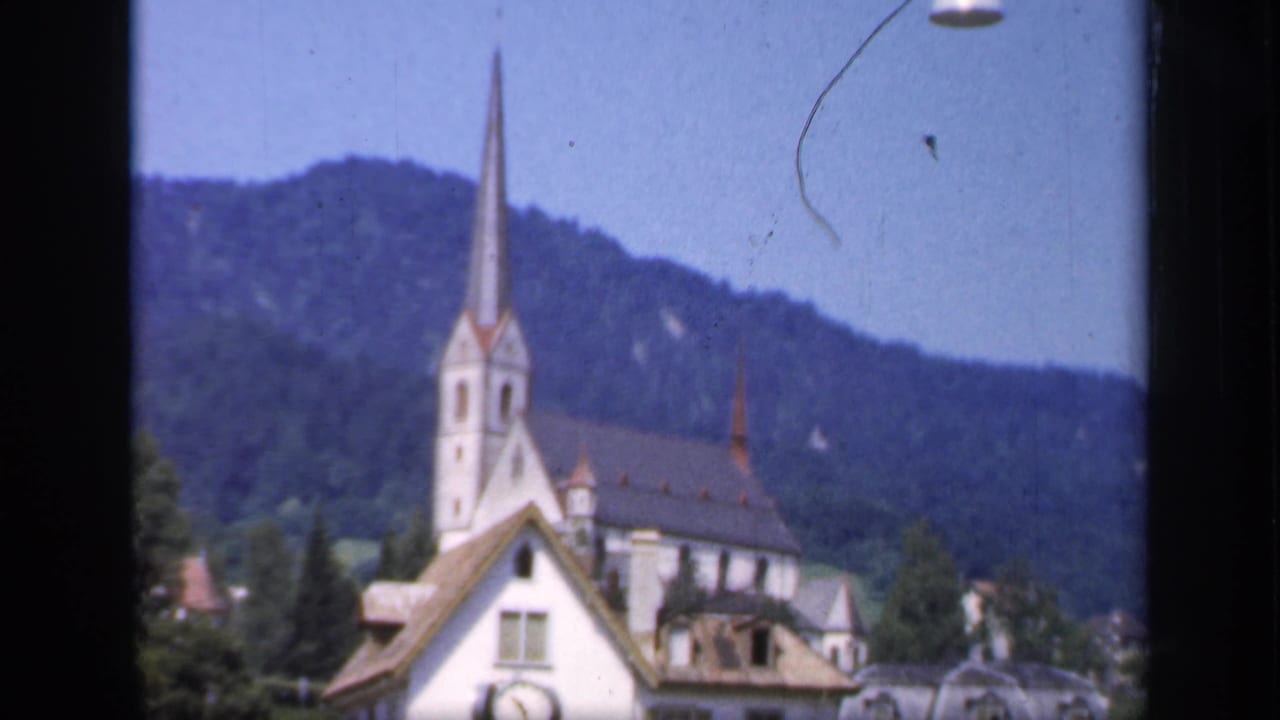 The camera holds on the church spire and surrounding village roofs, with wooded hills visible in the 1949 home-movie footage.