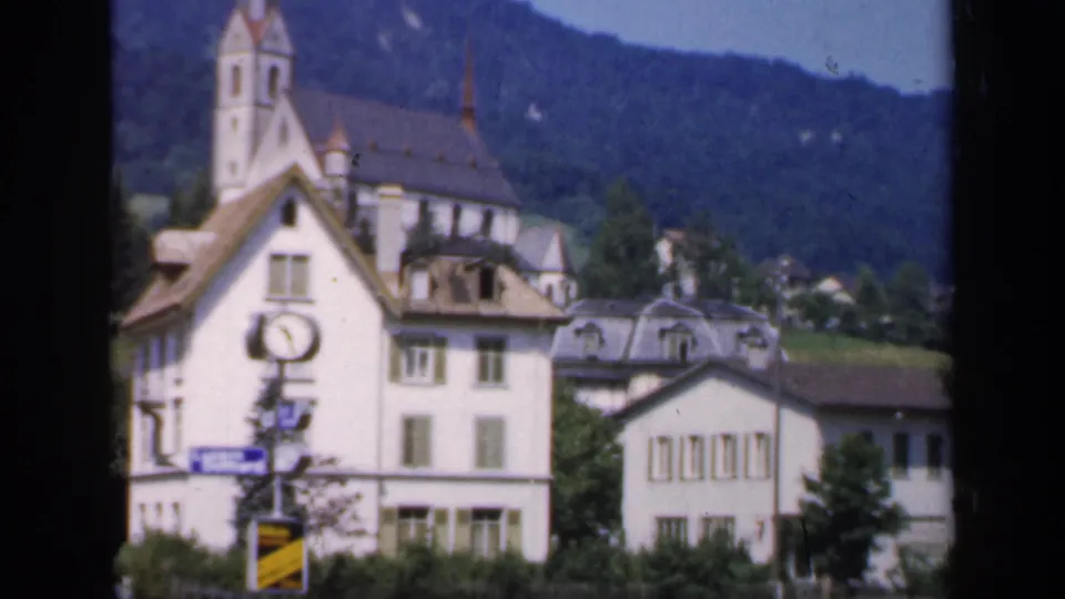 Soft 8mm view of a church spire, white village buildings, a foreground clock, and a green hillside, identified by metadata as England in 1949.