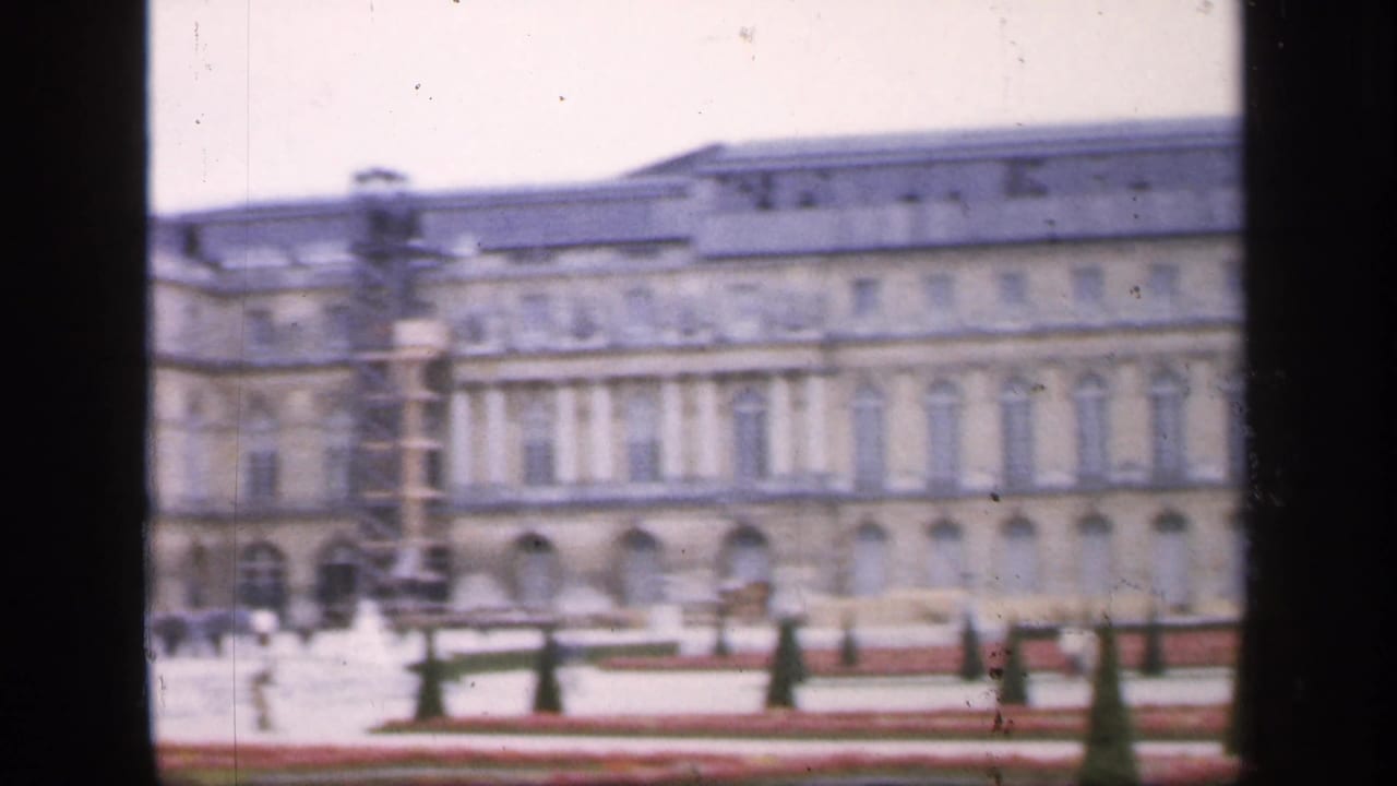 Soft 8mm view of the Palace of Versailles facade beyond formal garden beds.